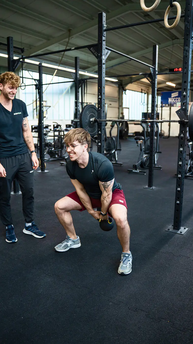 Patrick Keicher betreut einen Sportler bei einer Kniebeuge mit Kettlebell