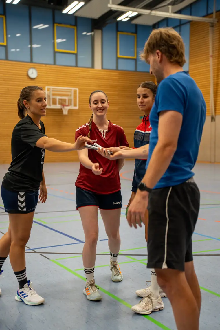 Patrick Keicher arbeitet in einer Sporthalle mit drei Handballspielerinnen
