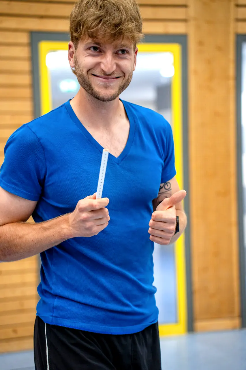 Patrick Keicher lächelt in die Kamera. Er trägt ein blaues T-Shirt und hält ein Lineal in der Hand.