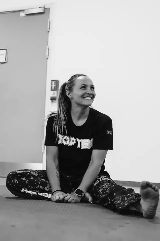 Stefanie Megerle sitzt lächelnd im Spagat, Schwarzweißaufnahme